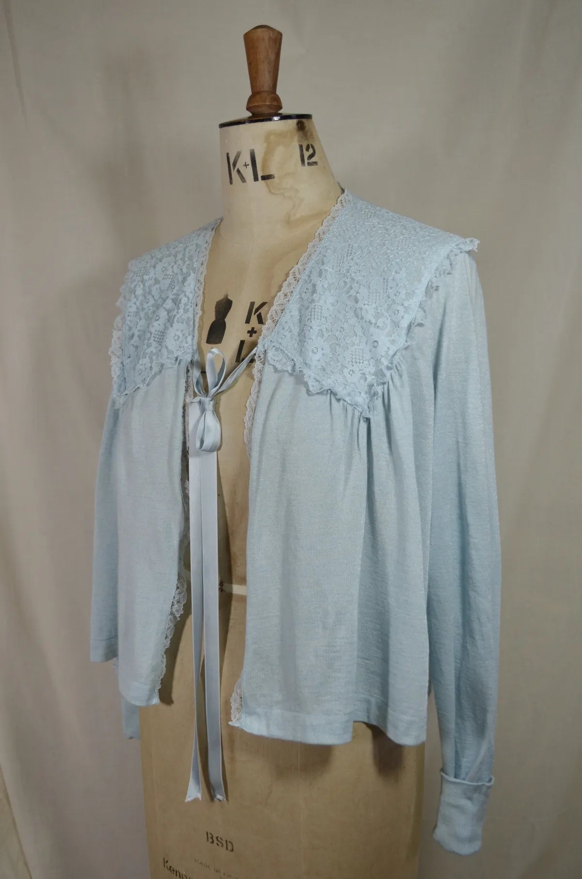 1930s Light blue lace-trimmed wool bed jacket on a mannequin against a beige background