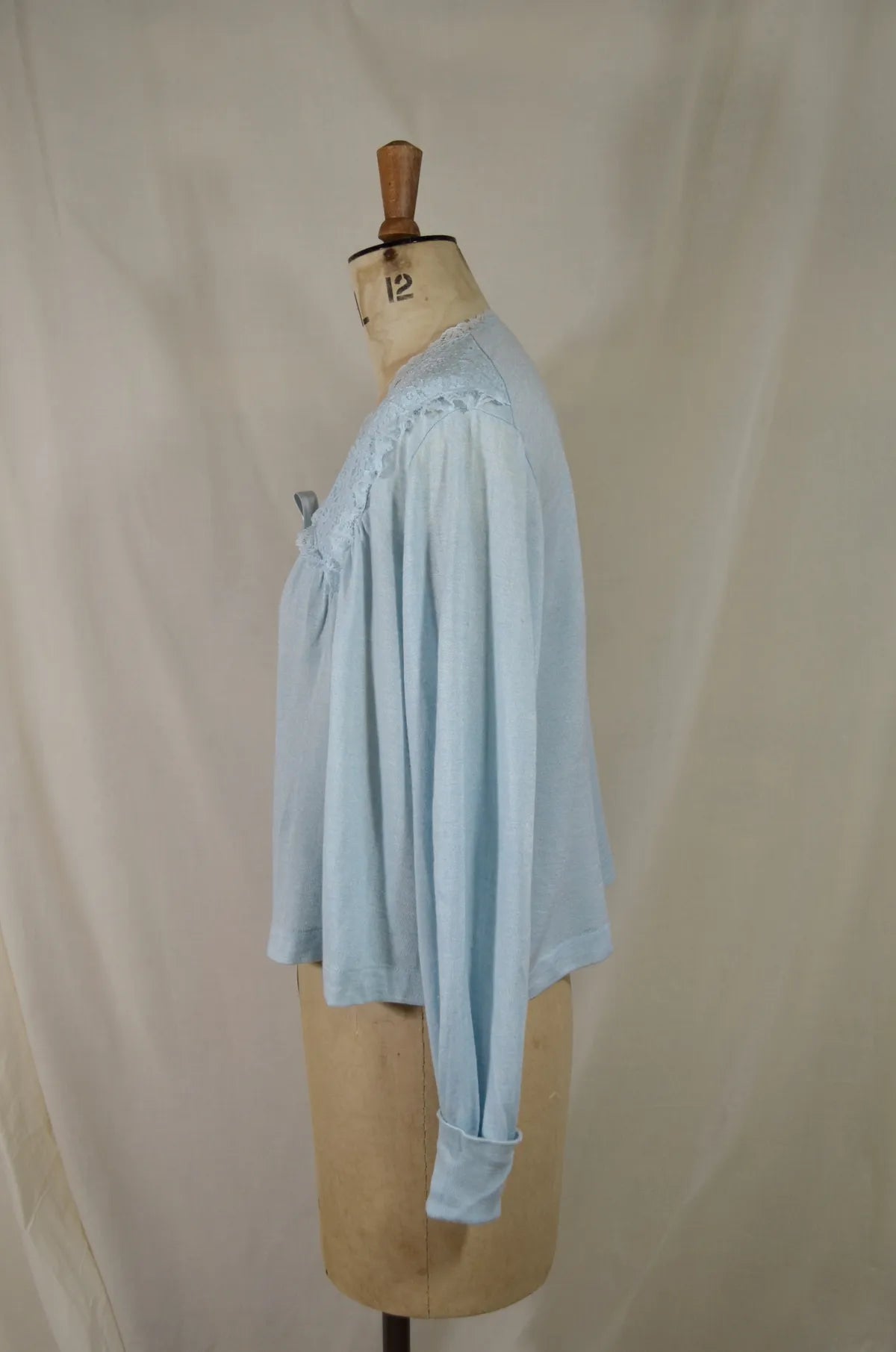 1930s Light blue lace-trimmed wool bed jacket on a mannequin against a beige background