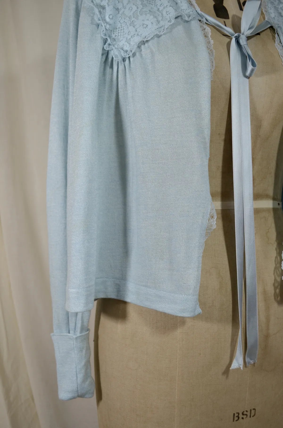1930s Light blue lace-trimmed wool bed jacket on a mannequin against a beige background