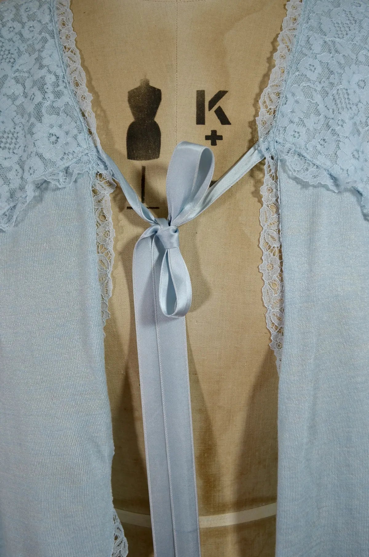 1930s Light blue lace-trimmed wool bed jacket on a mannequin against a beige background