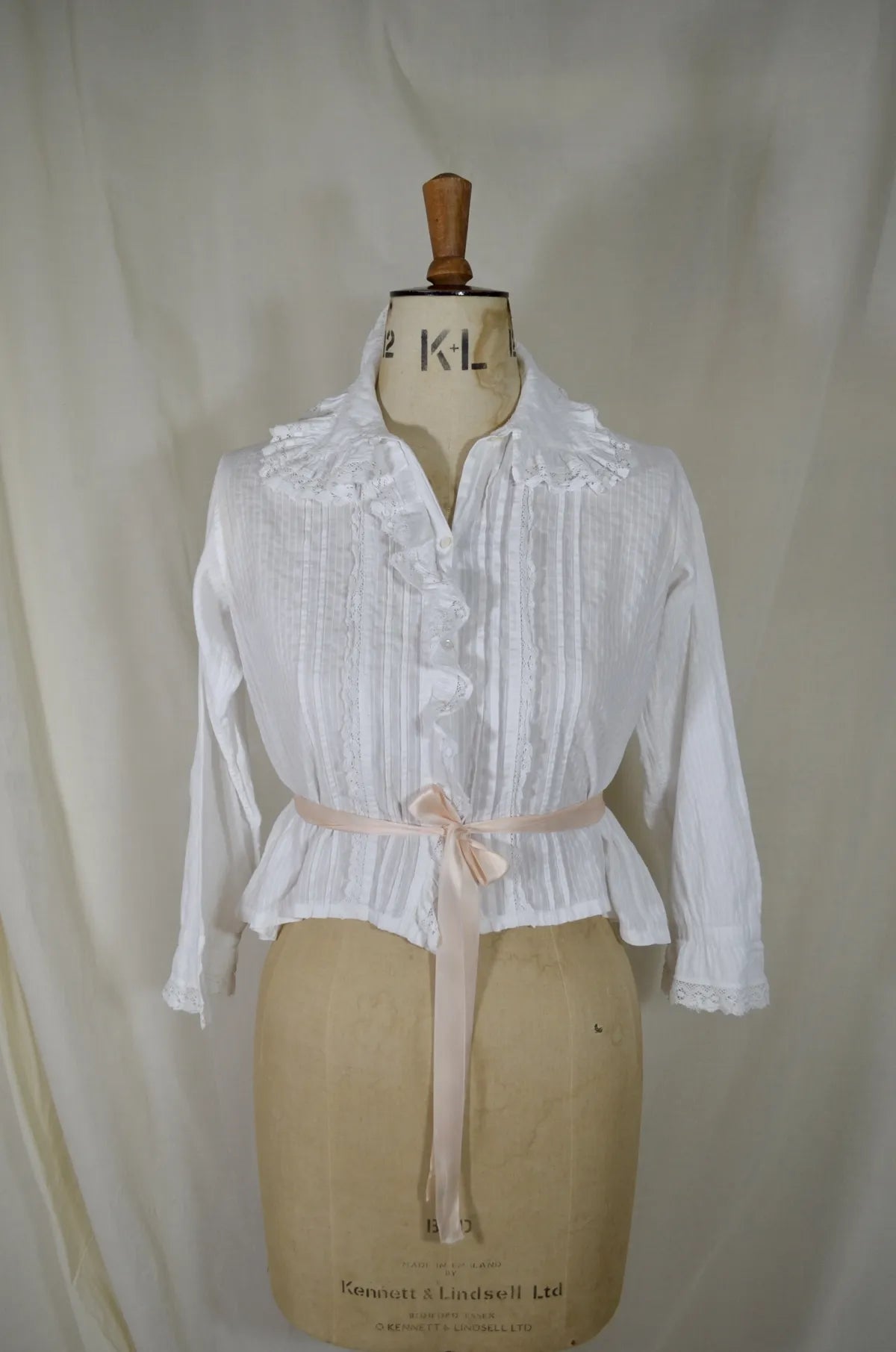 Victorian lace and cotton blouse with pink ribbon round waist on plain background