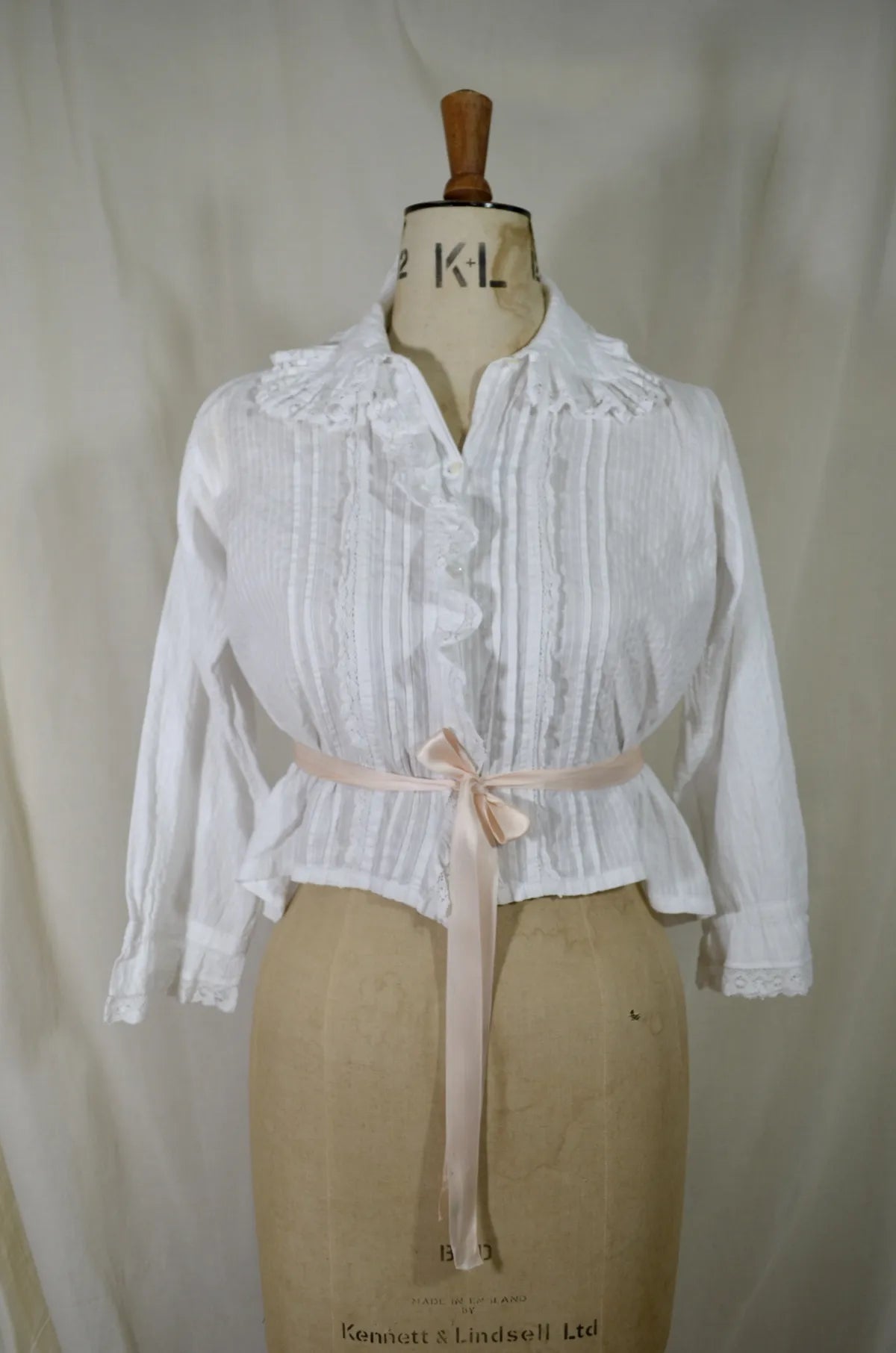 Victorian lace and cotton blouse with pink ribbon round waist on plain background
