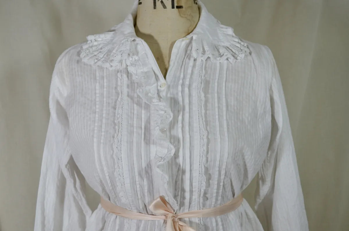 Victorian lace and cotton blouse with pink ribbon round waist on plain background