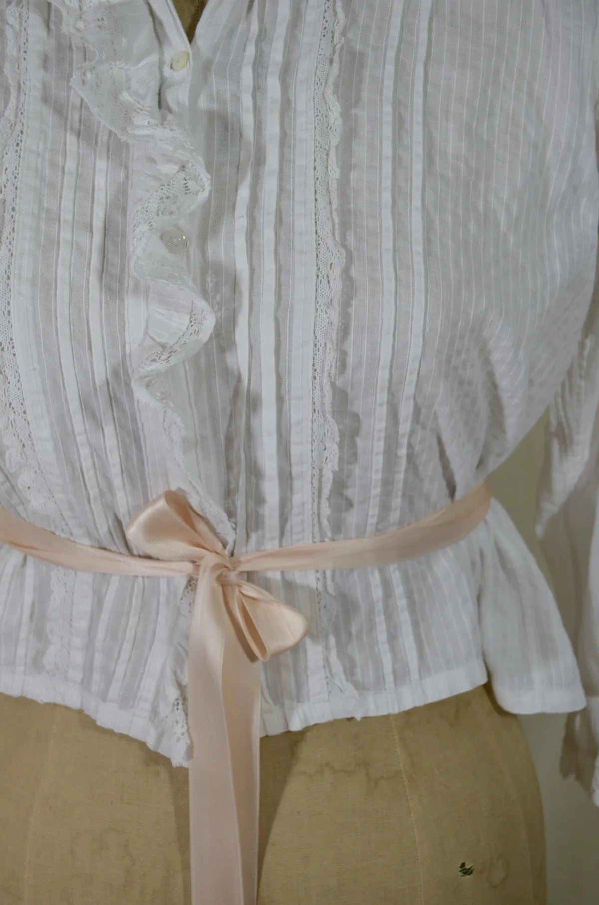 Victorian lace and cotton blouse with pink ribbon round waist on plain background