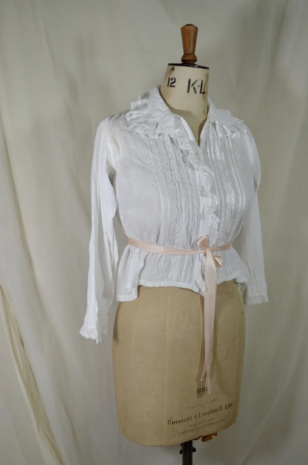 Victorian lace and cotton blouse with pink ribbon round waist on plain background