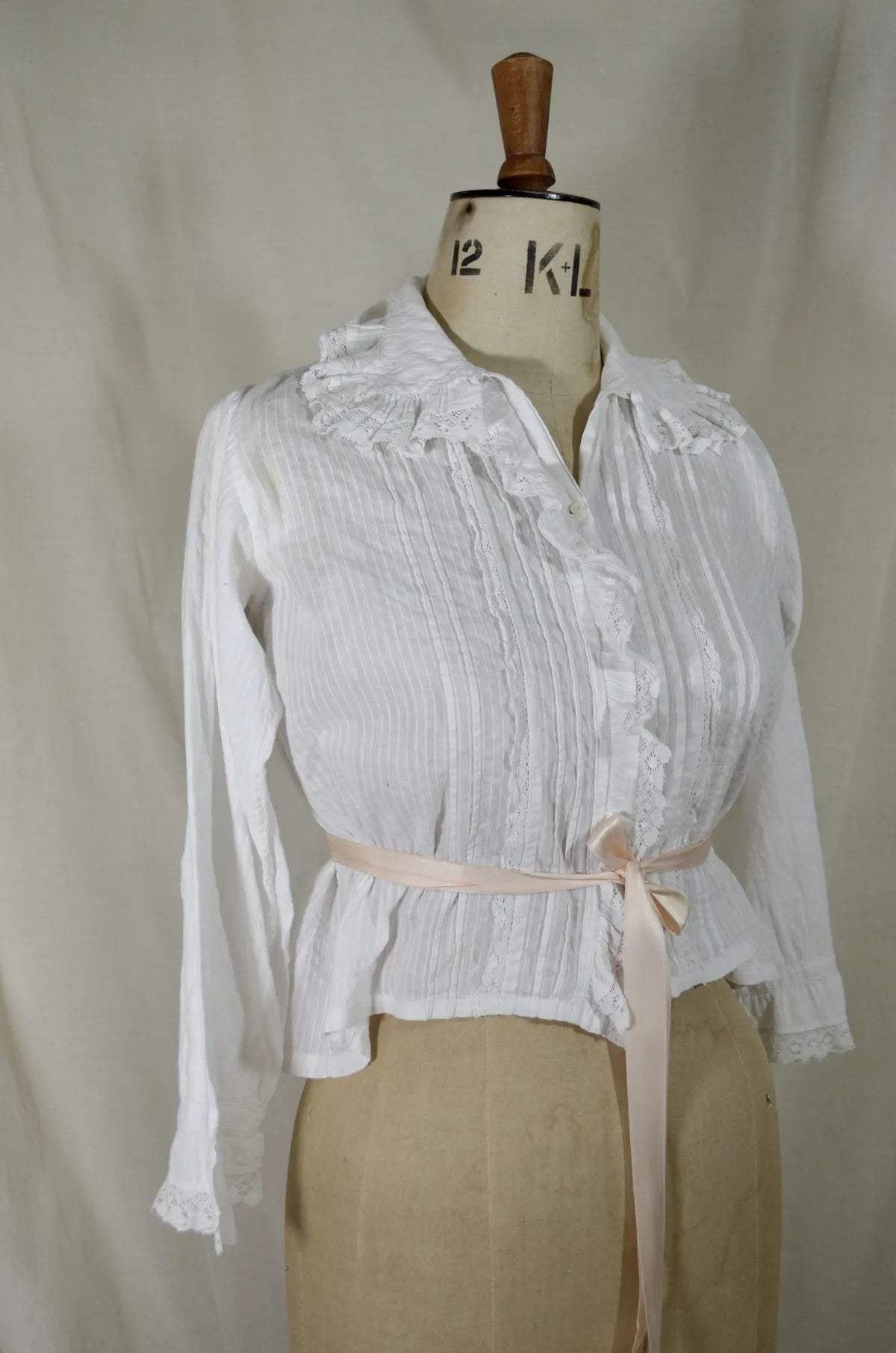 Victorian lace and cotton blouse with pink ribbon round waist on plain background