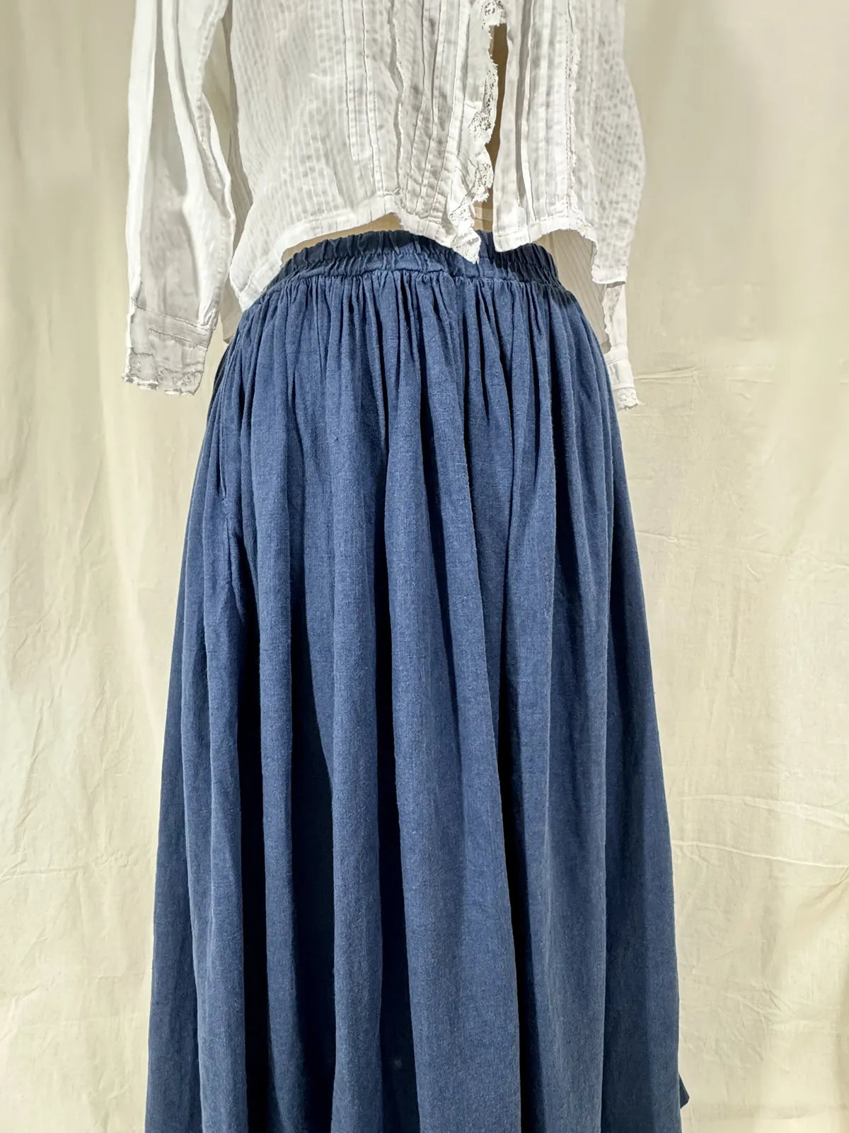 Blue skirt worn with a white blouse on a beige background