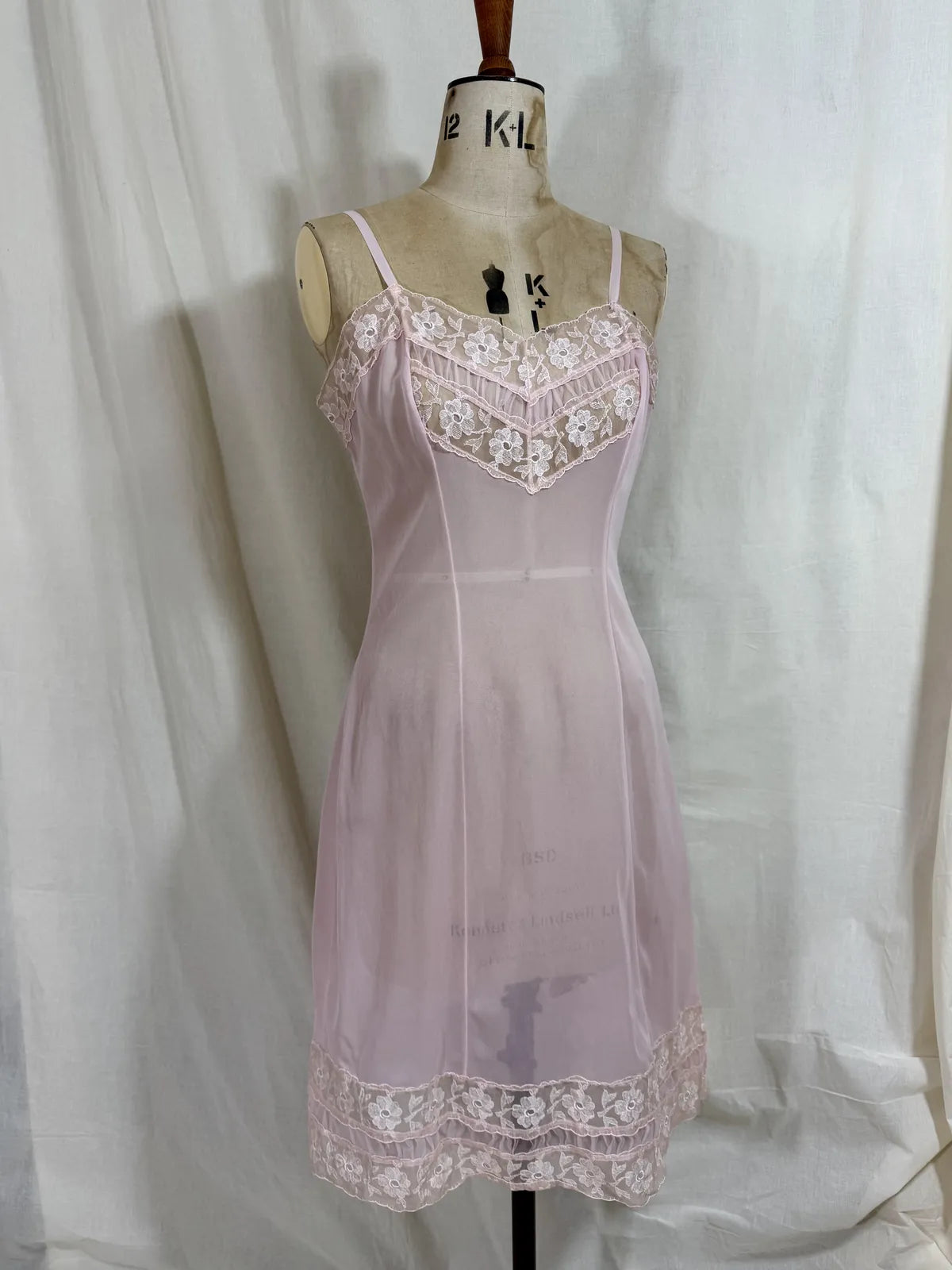 Pink slip dress with lace details on a mannequin against a white 