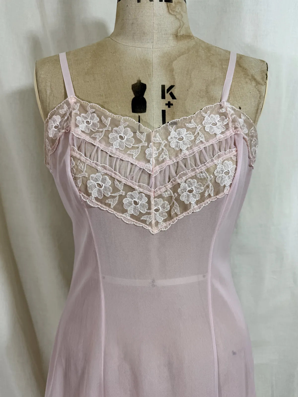 Pink slip dress with lace details on a mannequin against a white background