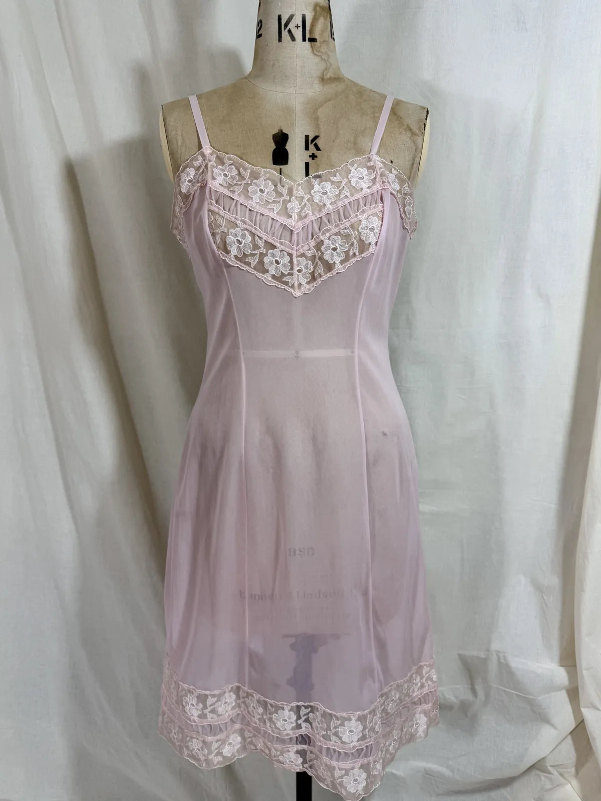 Pink slip dress with lace details on a mannequin against a white background
