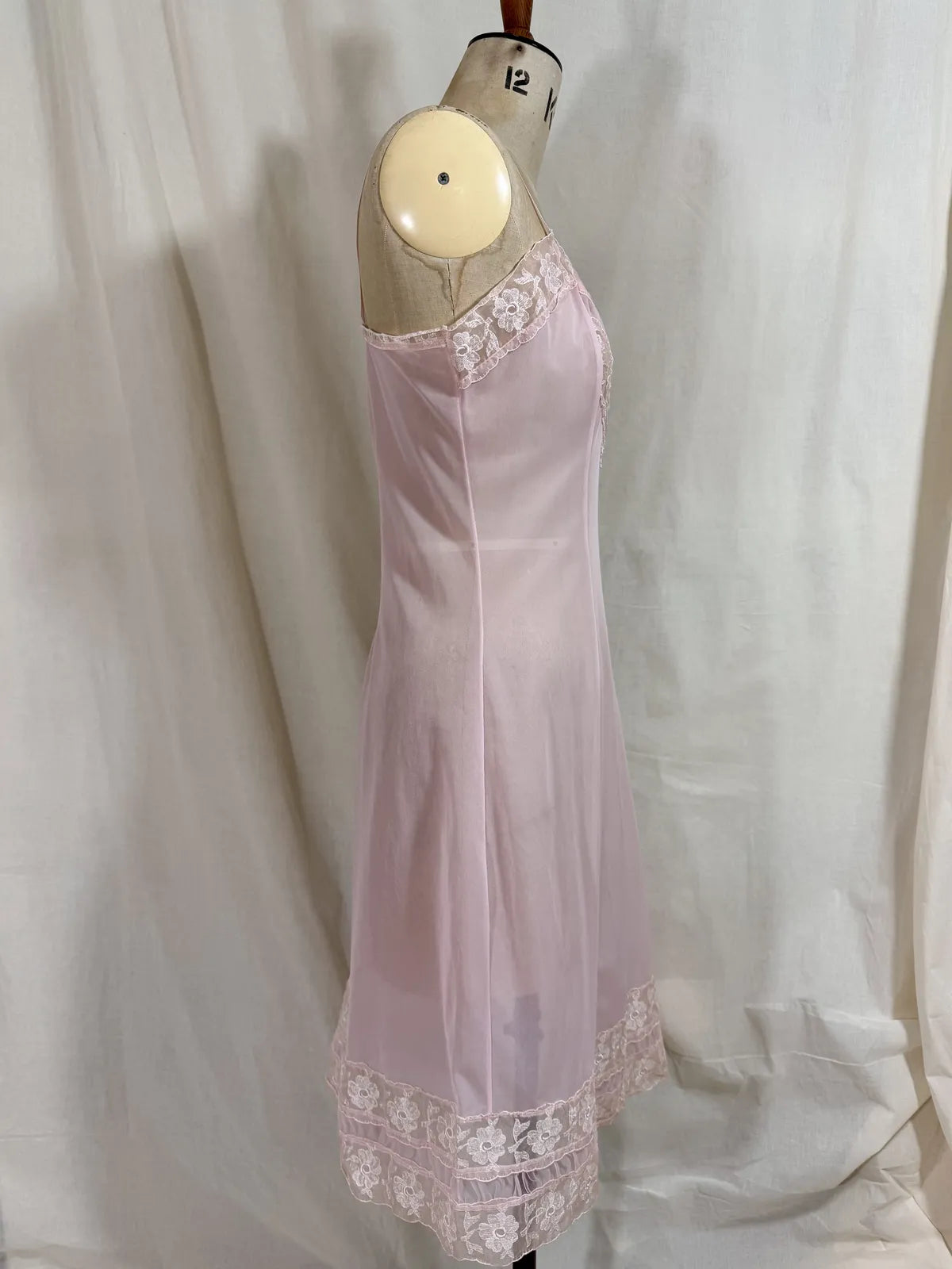 Pink slip dress with lace details on a mannequin against a white background