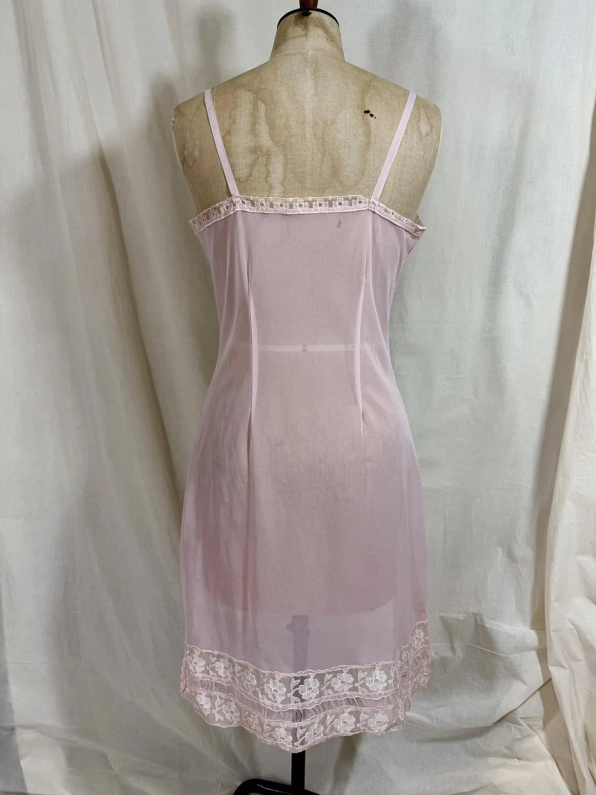 Pink slip dress with lace details on a mannequin against a white background