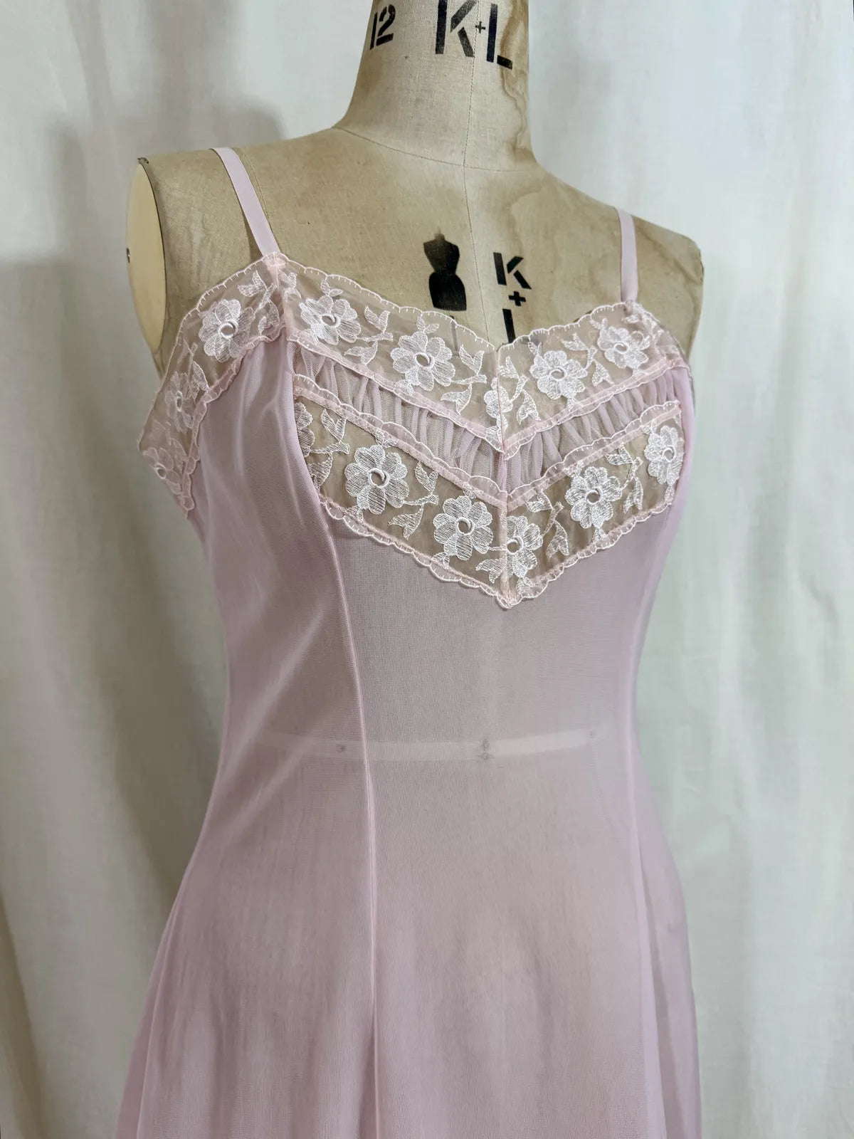 Pink slip dress with lace details on a mannequin against a white background