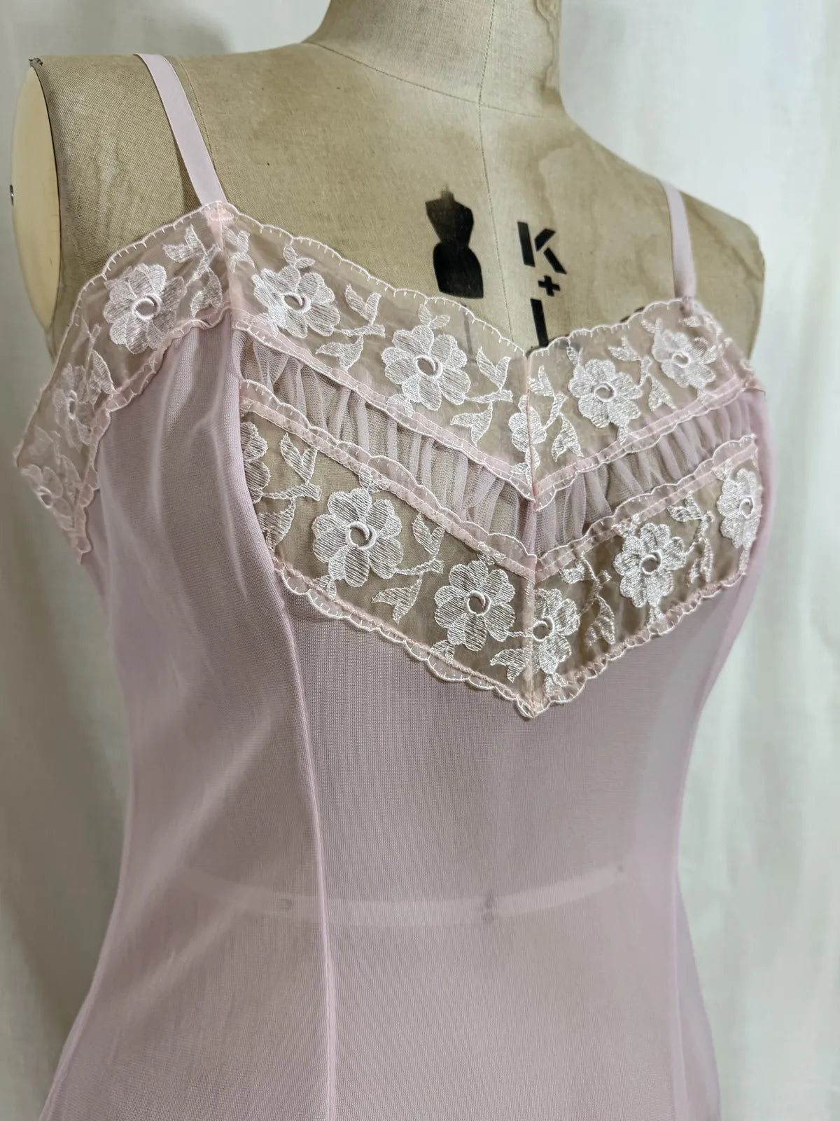 Pink slip dress with lace details on a mannequin against a white background