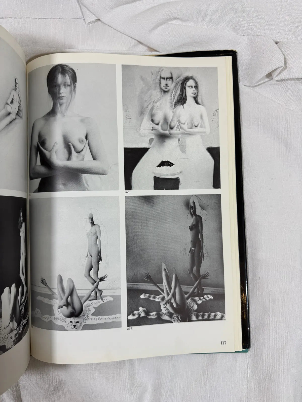 Open book displaying black and white images of nude figures on a white surface.