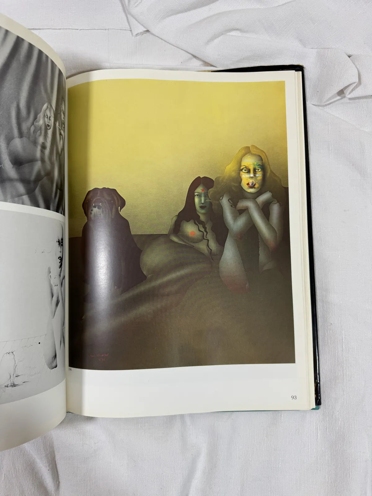 Open book with a surreal illustration of three figures on a white fabric background