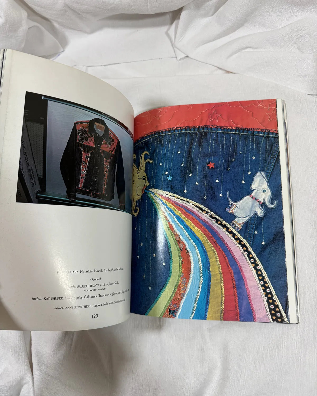 Open book showing a colorful embroidered garment with a rainbow design on a white fabric background